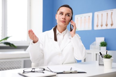 Photo of Doctor with smartphone having online consultation at table in clinic