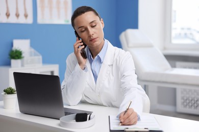 Photo of Doctor with smartphone having online consultation at table in clinic