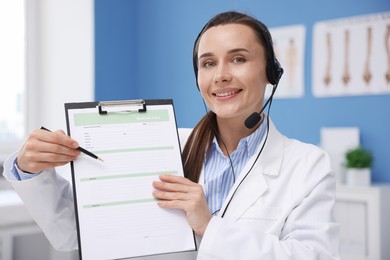 Photo of Doctor with headset and clipboard having online consultation in clinic