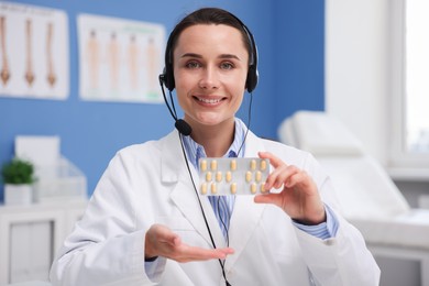 Photo of Doctor with headset and pills having online consultation in clinic