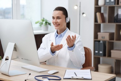 Photo of Doctor with headphones having online consultation via computer in clinic