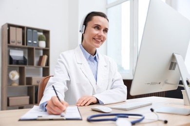 Photo of Doctor with headphones having online consultation via computer in clinic