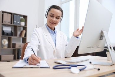 Photo of Doctor with headphones having online consultation via computer in clinic
