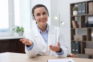 Photo of Doctor in headphones having online consultation at table indoors