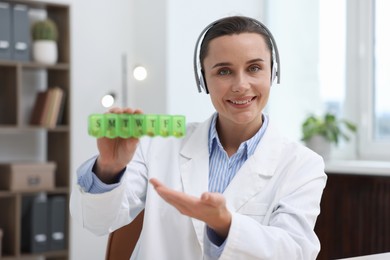 Photo of Doctor in headphones with pill box having online consultation indoors