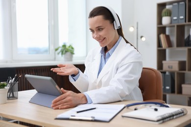 Photo of Doctor in headphones having online consultation via tablet indoors