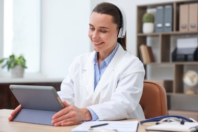 Photo of Doctor in headphones having online consultation via tablet indoors