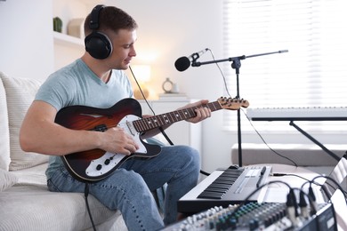 Photo of Man in headphones working with guitar and MIDI keyboard on sofa in home studio