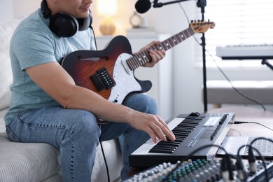 Photo of Man working with MIDI keyboard and guitar on sofa in home studio, closeup