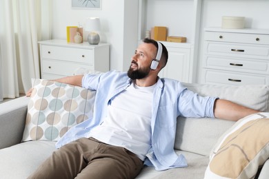 Photo of Harmony. Man listening to music in headphones on sofa at home