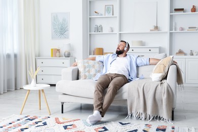 Photo of Harmony. Man listening to music in headphones on sofa at home