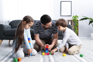 Photo of Father and his children playing with colorful cubes on floor at home