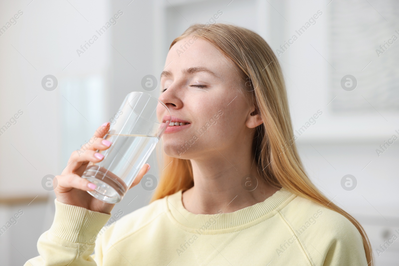 Young woman drinking water from glass at home Photo of Young woman drinking water from glass at home