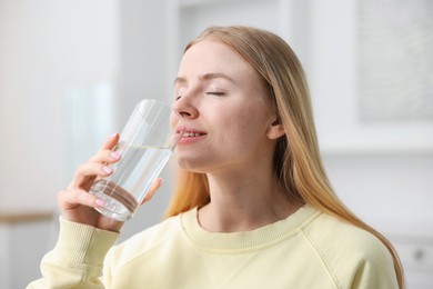Photo of Young woman drinking water from glass at home