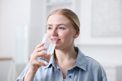 Photo of Young woman drinking water from glass at home