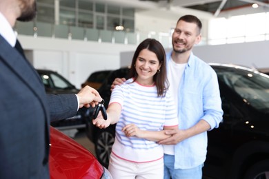 Photo of Salesman giving car key to happy family in salon, selective focus