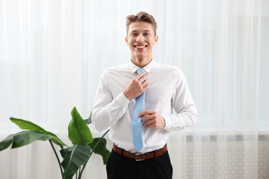 Photo of Man tying stylish blue necktie at home