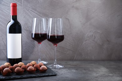 Photo of Tasty truffle bonbons and red wine on grey textured table, closeup. Space for text