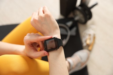 Photo of Woman checking fitness tracker during training indoors, closeup