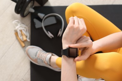 Photo of Woman checking fitness tracker during training indoors, closeup