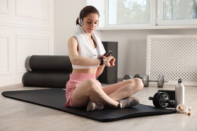 Photo of Woman checking fitness tracker during training indoors