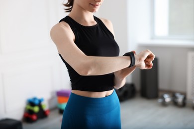 Photo of Woman checking fitness tracker during training indoors, closeup