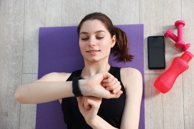 Photo of Woman checking fitness tracker during training indoors, top view