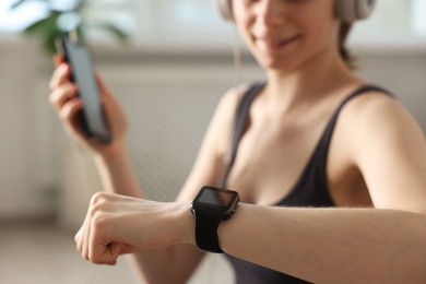 Photo of Woman checking fitness tracker during training indoors, closeup