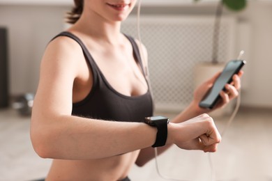Photo of Woman checking fitness tracker during training indoors, closeup