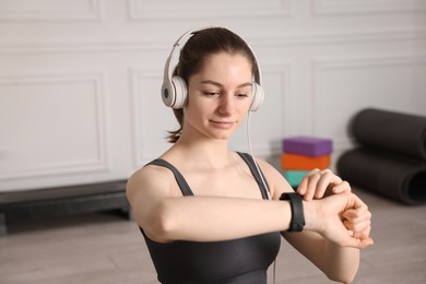 Photo of Woman checking fitness tracker during training indoors