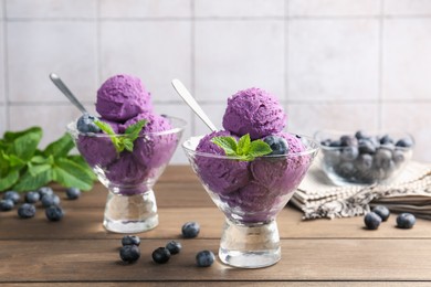 Photo of Tasty sorbet with blueberries and mint in dessert bowls on wooden table against tiled background, closeup