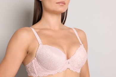 Photo of Woman wearing beautiful pink bra on light grey background, closeup