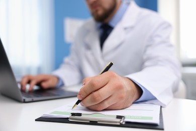 Photo of Doctor using laptop at table in clinic, selective focus. Online medical consultation