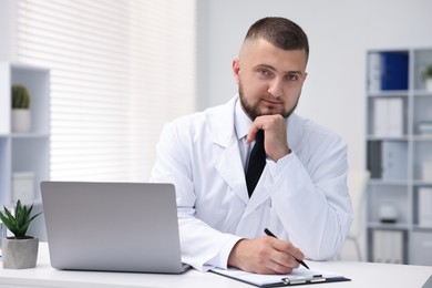 Photo of Doctor working at table with laptop in clinic. Online medical consultation