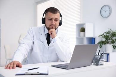 Photo of Doctor in headphones having online consultation via laptop indoors