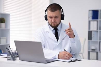 Photo of Doctor in headphones having online consultation via laptop indoors