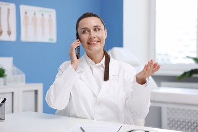 Photo of Doctor with smartphone having online consultation at table in clinic