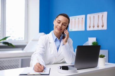 Photo of Doctor with smartphone having online consultation at table in clinic