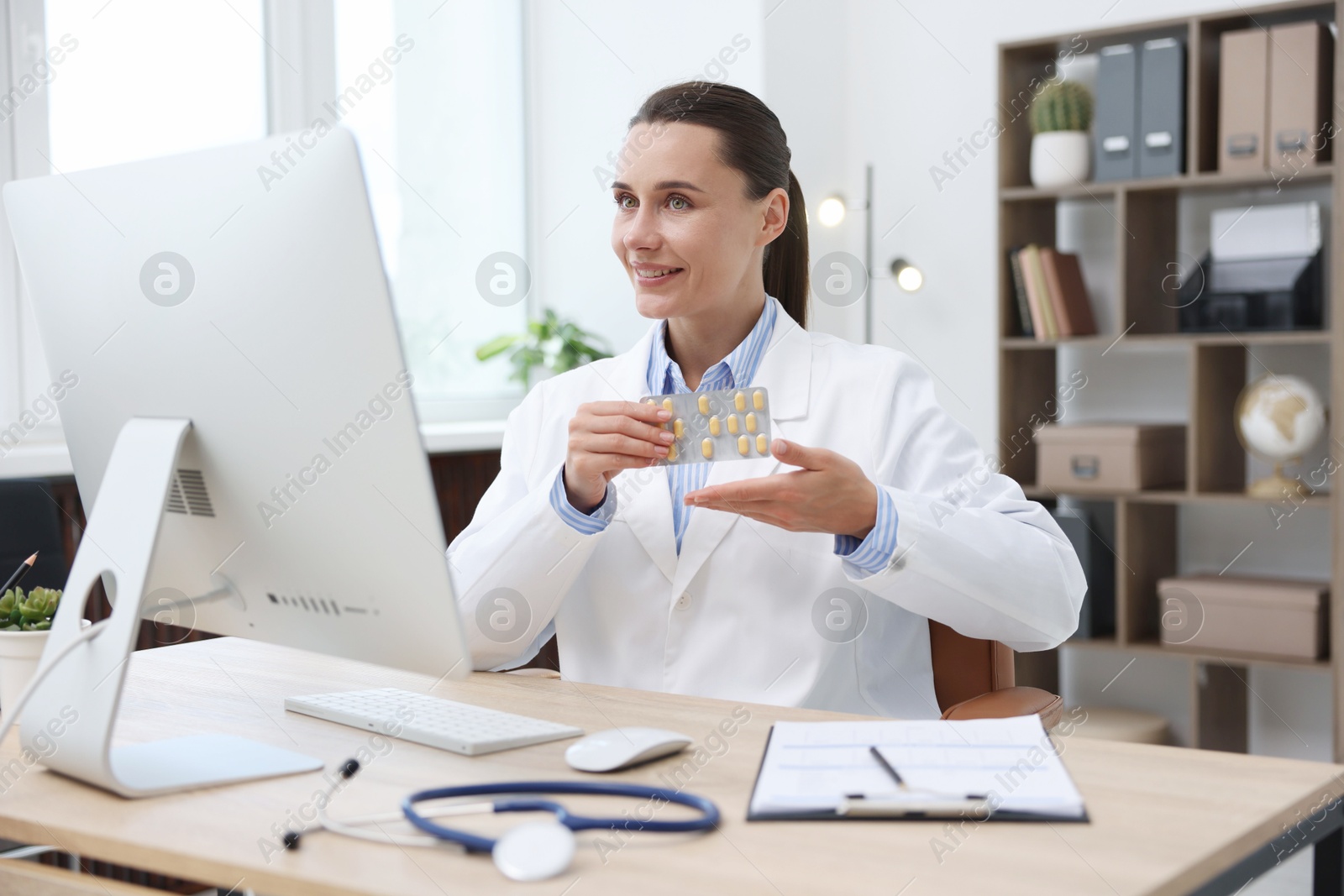 Doctor with pills having online consultation via computer in clinic Photo of Doctor with pills having online consultation via computer in clinic