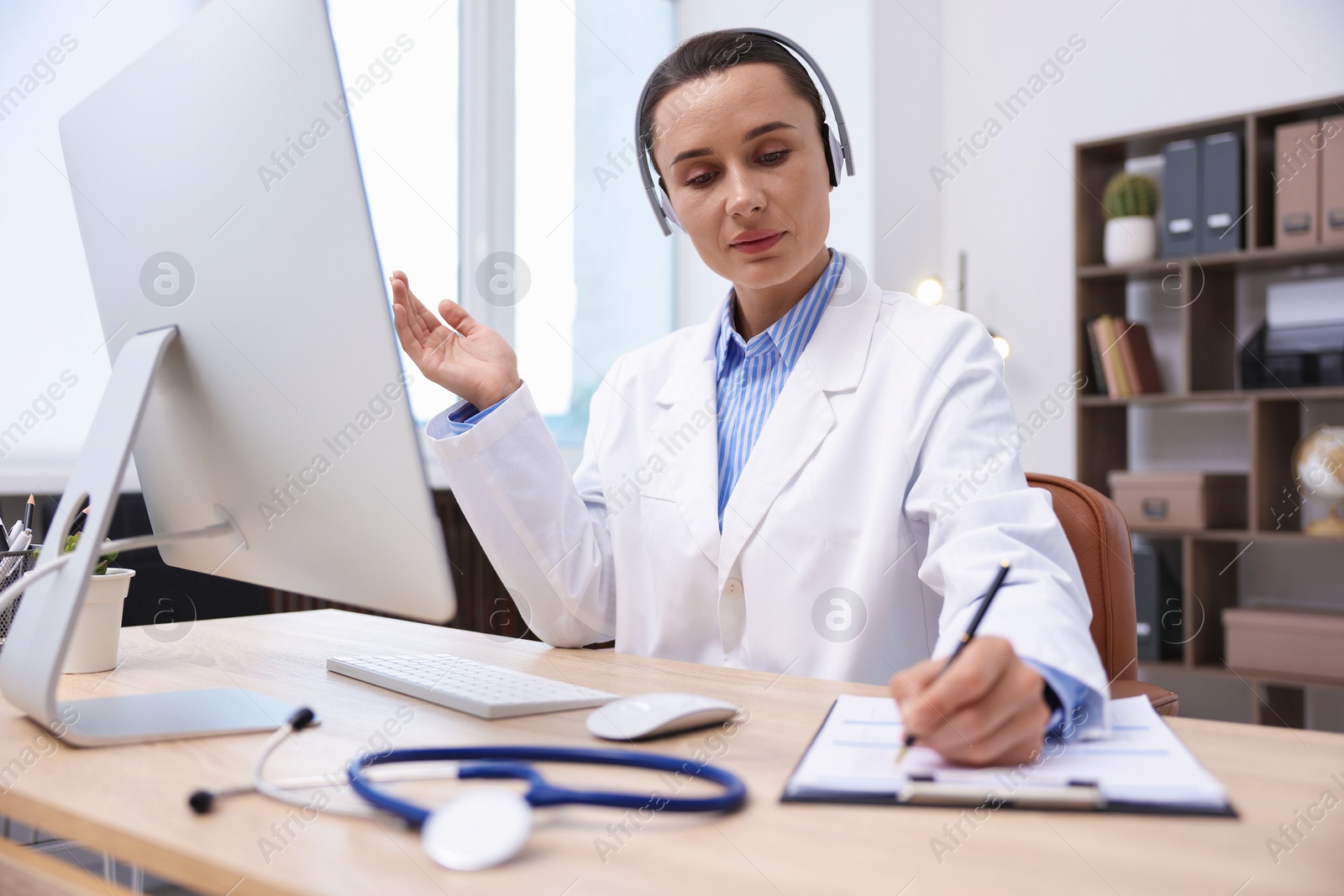 Photo of Doctor with headphones having online consultation via computer in clinic