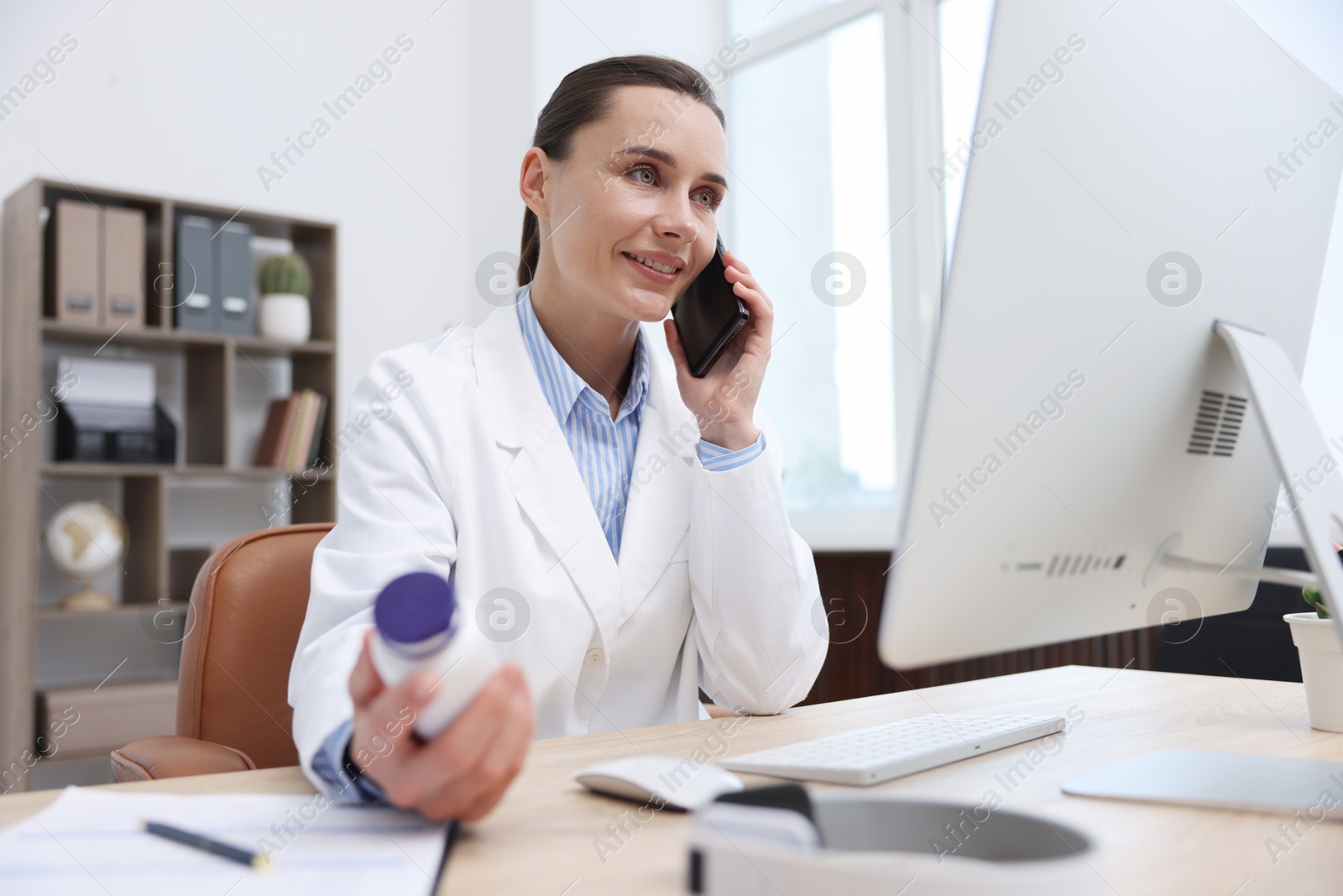 Doctor with smartphone and pills having online consultation in clinic Photo of Doctor with smartphone and pills having online consultation in clinic