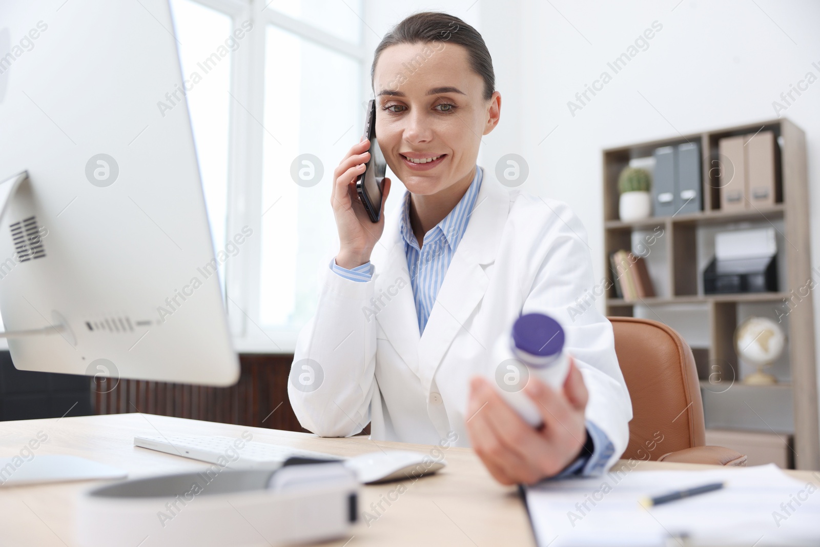 Doctor with smartphone and pills having online consultation in clinic Photo of Doctor with smartphone and pills having online consultation in clinic