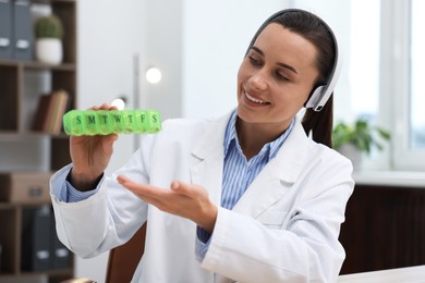 Photo of Doctor in headphones with pill box having online consultation indoors
