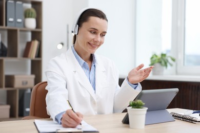 Photo of Doctor in headphones having online consultation via tablet indoors