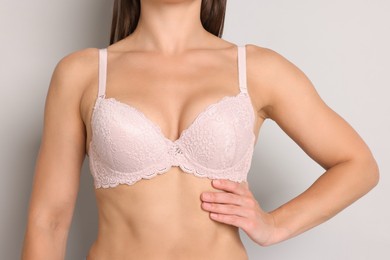 Photo of Woman wearing beautiful pink bra on light grey background, closeup