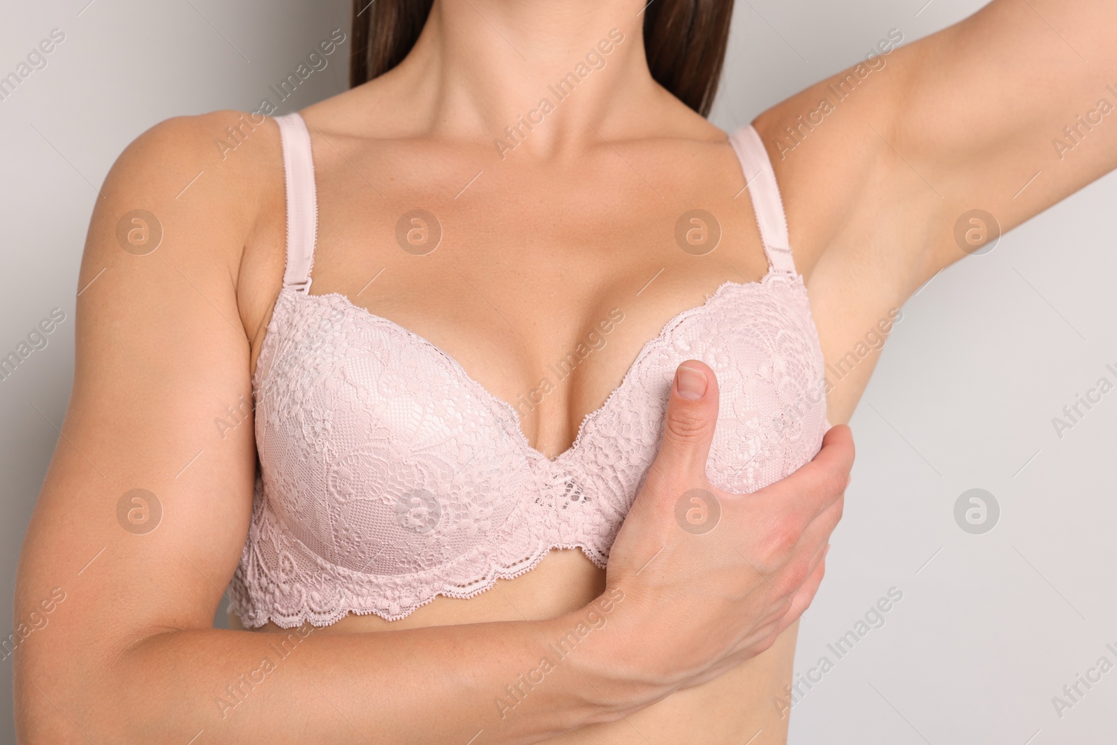 Photo of Woman wearing beautiful pink bra on light grey background, closeup