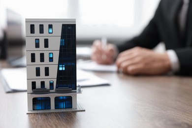 Photo of Real estate agent working at desk in office, focus on house model