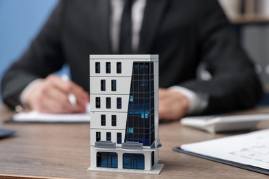 Photo of Real estate agent working at desk in office, focus on house model
