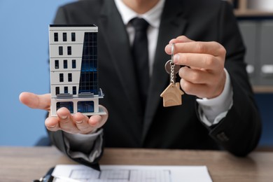 Photo of Real estate agent holding house model and key at desk in office, closeup