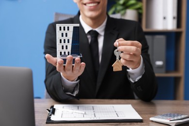 Photo of Real estate agent holding house model and key at desk in office, closeup